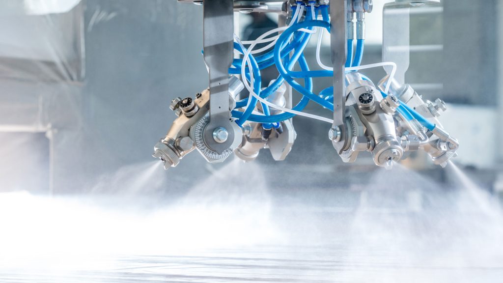 Close-up of a robotic spraying system with multiple nozzles emitting fine mist, featuring blue and white hoses connected to the machinery, perfect for modernizing luxury bespoke kitchens in the UK.