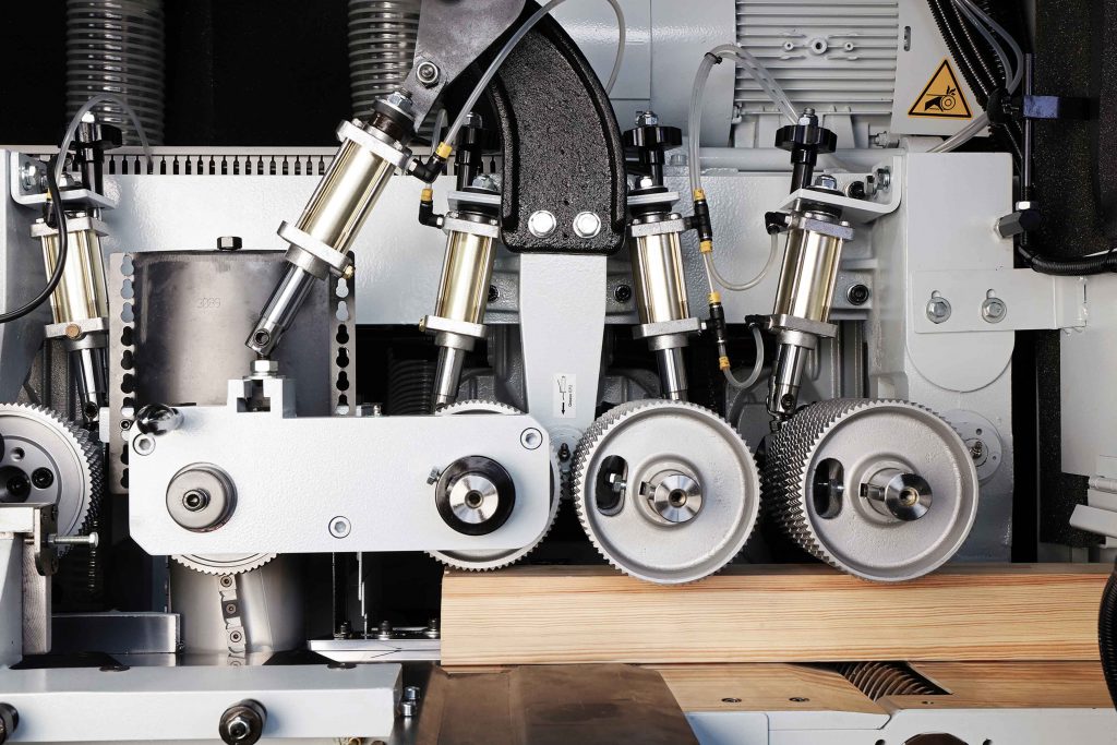 Close-up of an industrial woodworking machine in operation, with multiple gears and rollers processing a piece of wood for a luxury kitchen renovation.