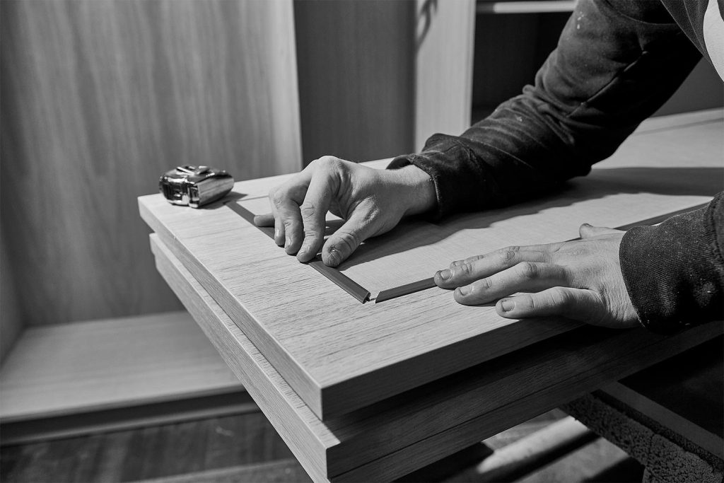 A person is meticulously measuring and aligning wooden boards with a measuring tape on a workbench, preparing for a bespoke luxury kitchen renovation.
