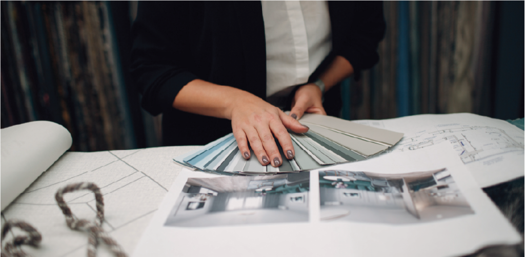 A person holding a color swatch book over a table with architectural plans and two photos of bespoke luxury kitchens.