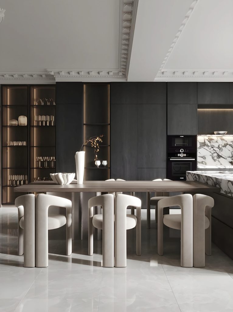 A modern kitchen with sleek dark cabinetry, marble countertops, a built-in oven, and a dining table surrounded by six minimalist chairs. Decorative items are displayed on shelves. Perfect for those seeking luxury bespoke kitchens in the UK.