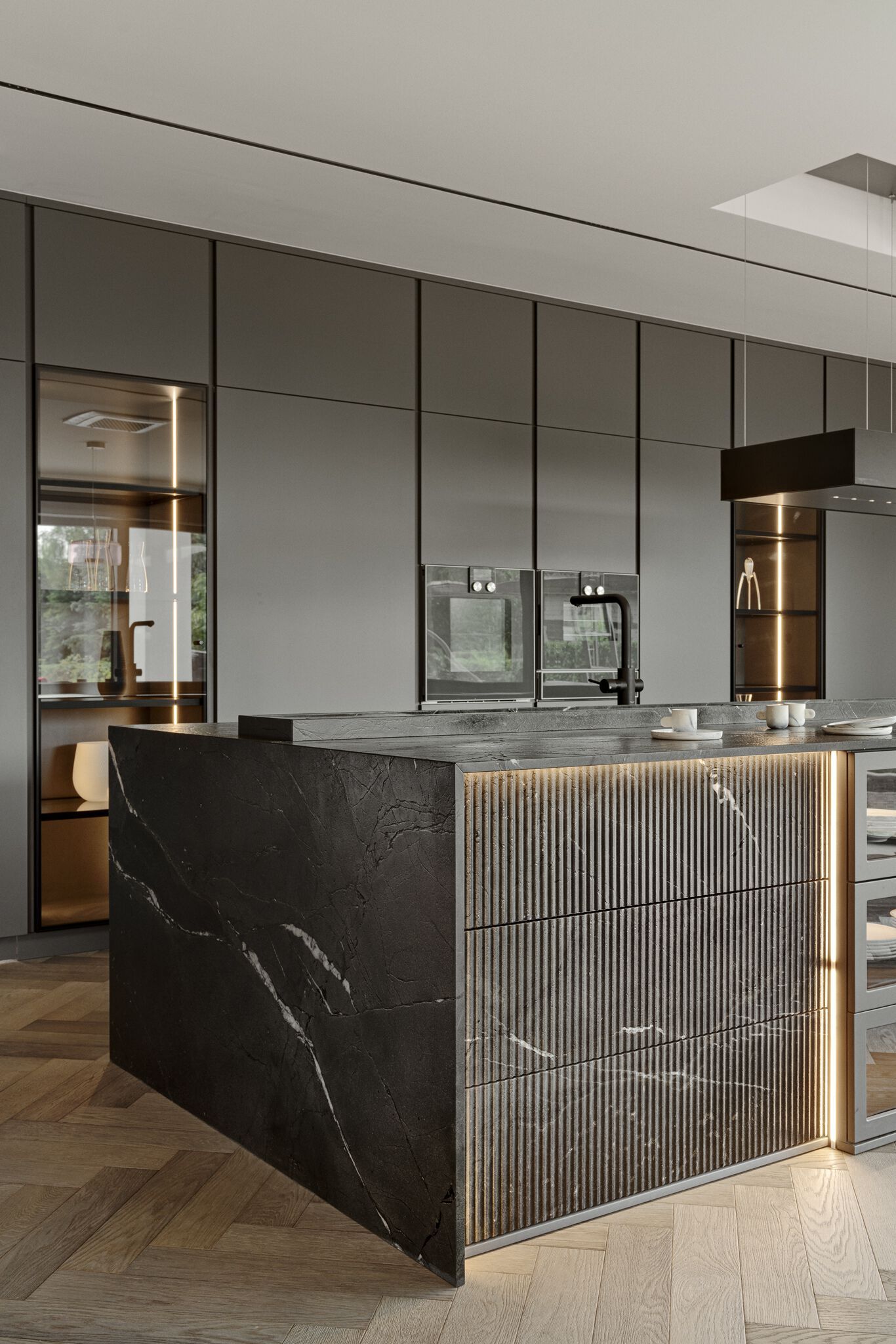 Modern kitchen with sleek gray cabinetry, black marble countertop island, and wooden herringbone flooring. Recessed lighting highlights textured island panels.