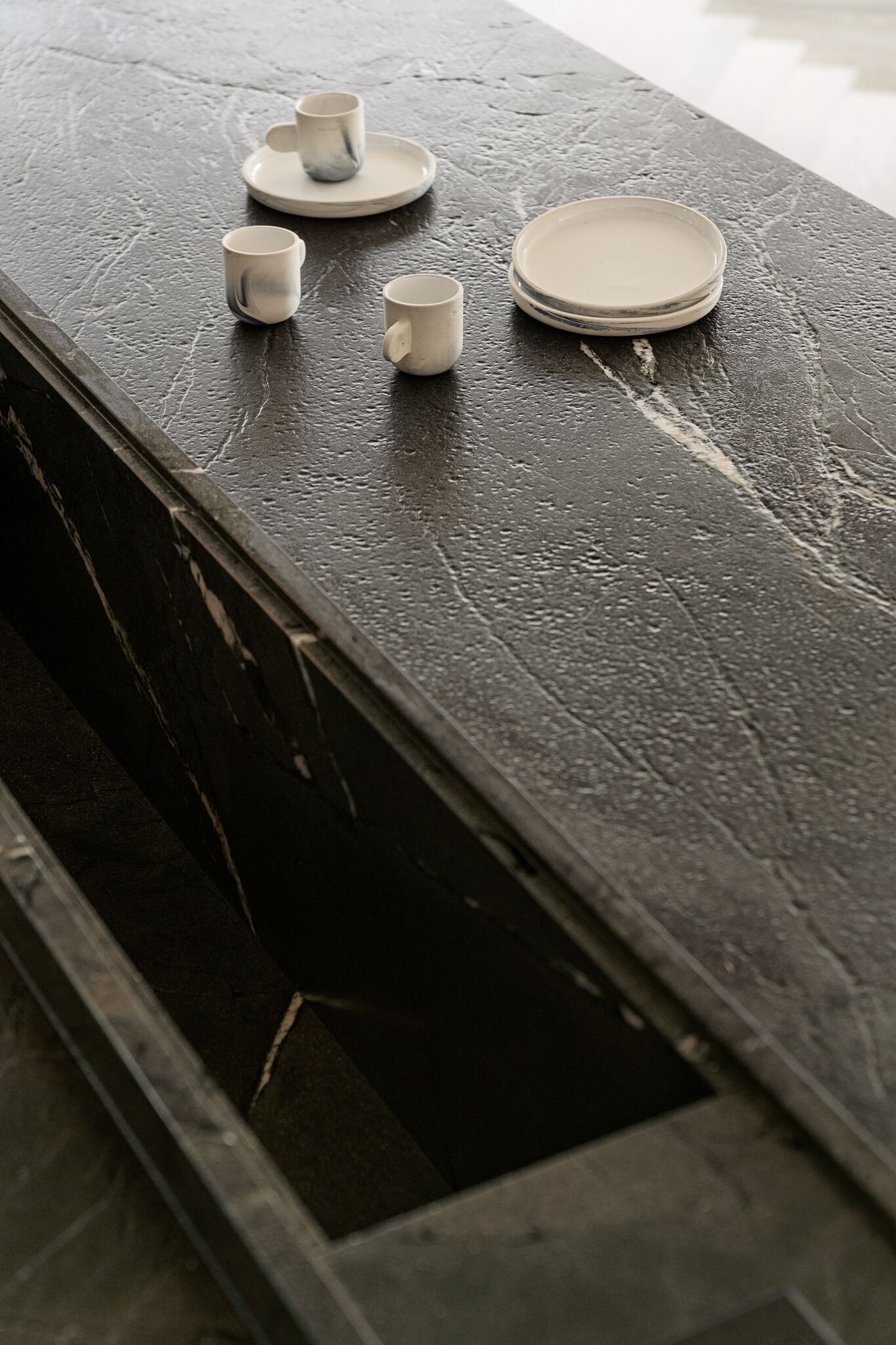 Four white cups and a stack of white plates sit on a dark, textured countertop.