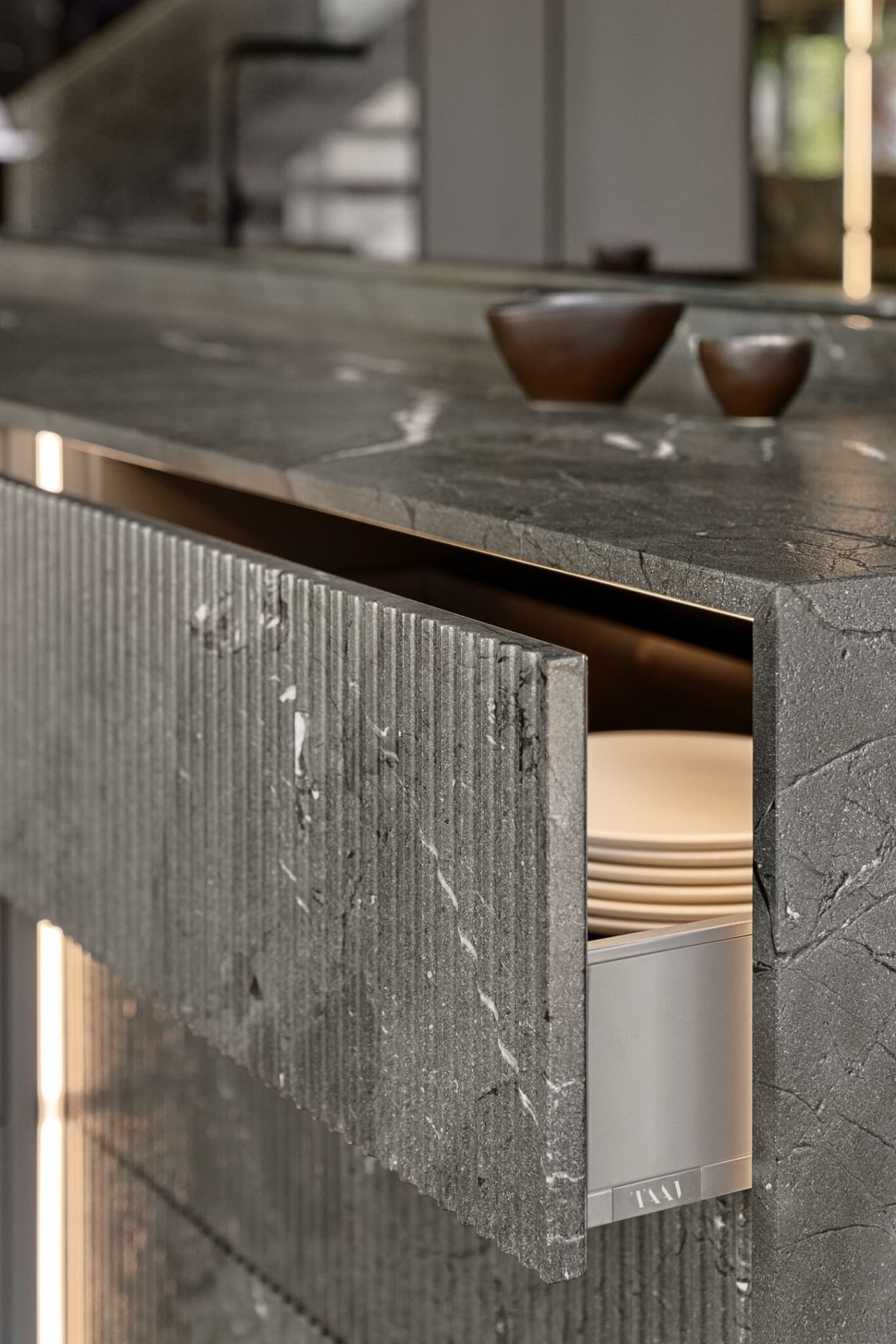 A stone-textured kitchen drawer, partially open, reveals stacked white plates. Two small brown cups are on the countertop above.
