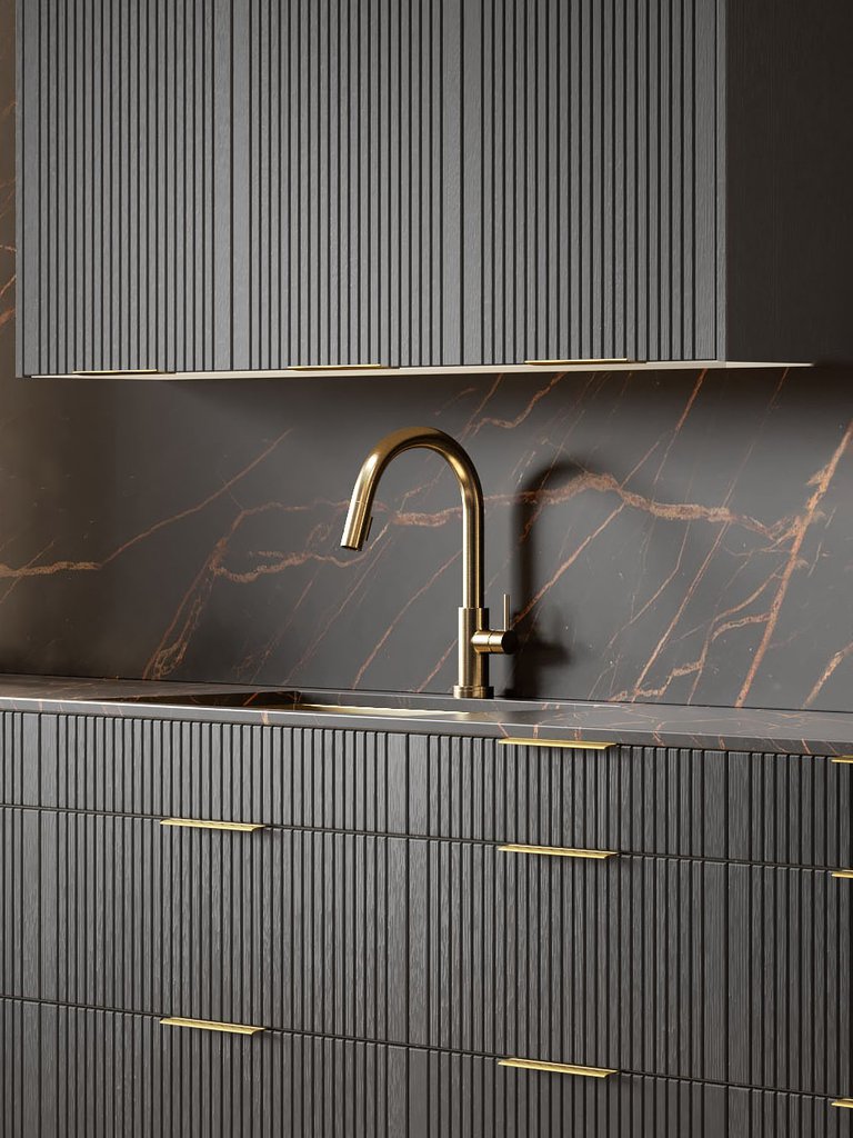 Modern kitchen with dark cabinetry featuring vertical grooves, gold handles, and a gold faucet. Marble backsplash with subtle vein patterns in the background.